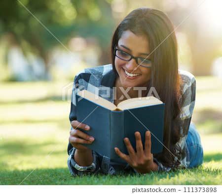 Happy woman, student and reading book on green grass for literature, studying or story in nature. Female person, smart or young adult with smile or glasses for chapter, learning or education at park 111373898
