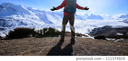 Woman hiker enjoy the view on mountain top cliff edge face to glacier mountains 111374929