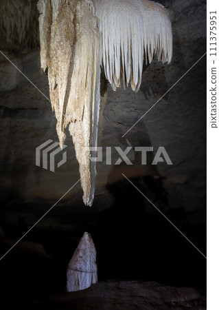 Majestic Stalactite and Stalagmite Formation in a Dark Cave 111375951