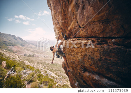 Rock climbing, rope and fearless mountain climber on a cliff, big rocks and risky challenge alone in summer. Mountaineering, bouldering and strong man training his body for balance outdoors in nature 111375989