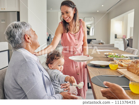 Mom, baby and grandmother eating at table, bonding and sharing food and love at home. Happy, smile and relax women bonding while having a meal, enjoying family time and being loving and caring 111376435