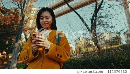 Japanese woman, city and phone for typing on social media, scroll notification and download digital app outdoor. Happy urban commuter with smartphone technology to search for travel location in Tokyo 111376580