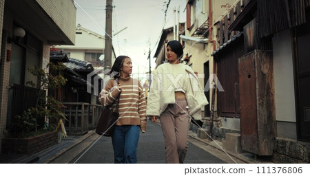 Japanese women, friends and walk in city, talking and travel together on vacation, street and buildings. People, girl and outdoor in metro road, houses or urban neighborhood in conversation in Tokyo 111376806