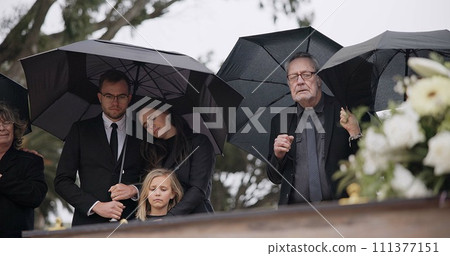 Death, funeral and umbrella, people at coffin for service in graveyard in respect, mourning and support. Flowers, rain and loss, family at casket in cemetery with memory, grief and grave for burial. 111377151