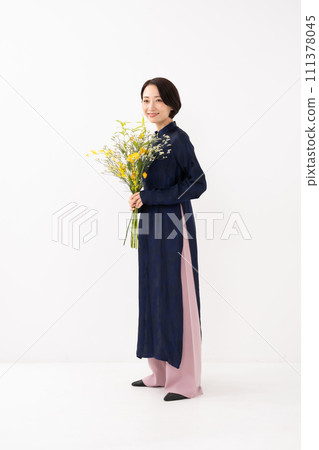 A woman wearing an ao dai and holding a bouquet of flowers 111378045