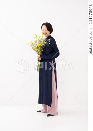 A woman wearing an ao dai and holding a bouquet of flowers 111378048