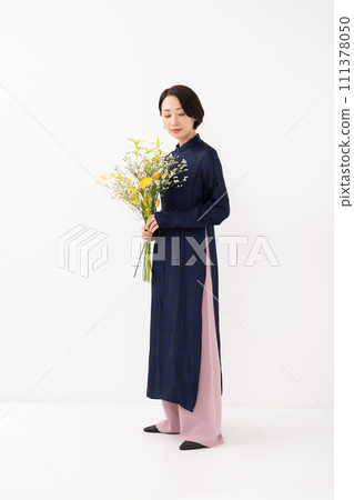 A woman wearing an ao dai and holding a bouquet of flowers 111378050