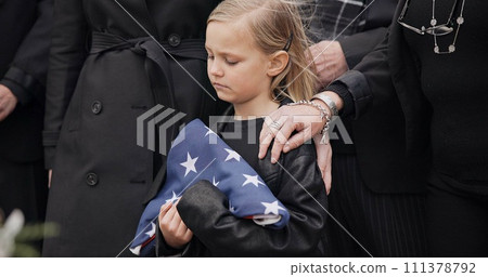 Funeral, cemetery and girl with American flag for veteran for respect, ceremony and memorial service. Family, depression and sad child by coffin in graveyard mourning military, army and soldier hero 111378792