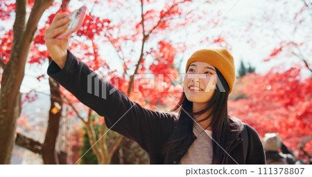 Japanese, woman and selfie in autumn nature with trees, leaves or travel to forest in Kyoto. Red, rainforest and girl smile with smartphone in fall environment with colorful woods and zen garden 111378807