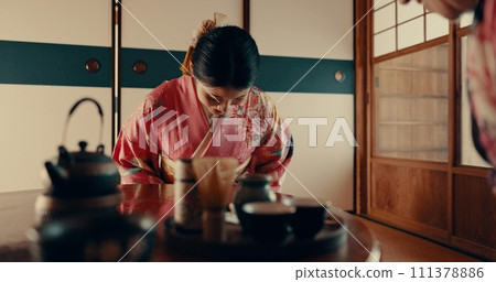 Woman in Japanese tea house with bow, kimono and relax with mindfulness, respect and gratitude. Girl at calm tearoom for matcha drink, zen culture and ritual at table for traditional ceremony in home 111378886