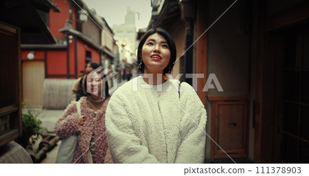 Women, friends and walk in street, talking and travel together on vacation, city and buildings. Japanese people, girl and chat outdoor in metro road, houses and urban neighborhood with ideas in Tokyo 111378903