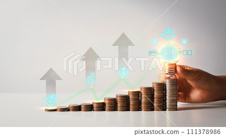 Hand holding glowing light bulb over coin stack with up arrow icons. Income management concepts 111378986