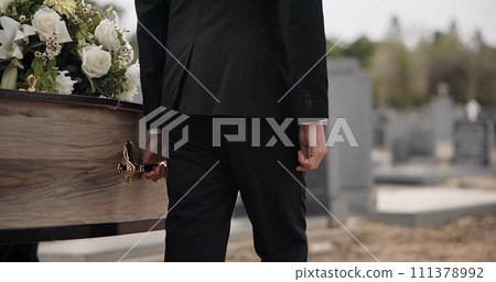 Coffin, hands and man walking at funeral ceremony outdoor with pallbearers at tomb. Death, grief and person carrying casket at cemetery, graveyard or family service of people mourning at windy event 111378992