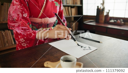 Hands, writing and Japanese woman for traditional script on paper, documents and letters in home. Creative, Asian culture and person with paintbrush tools for calligraphy, font and text in house 111379092