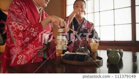 Japanese, women and kimono for tea ceremony in Chashitsu room with peace or custom tradition. People, temae and vintage style dress or talking with culture, fashion and honor with antique crockery Japanese, women and kimono for tea ceremony in Chashitsu room with peace or custom tradition. People, temae and vintage style dress or talking with culture, fashion and honor with antique crockery 111379149