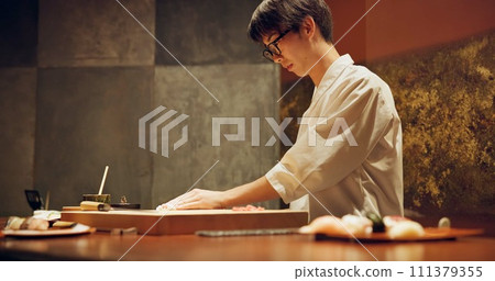 Chef, restaurant or japanese sushi as fish, raw salmon or healthy food for local culture in kitchen. Asian man, hands and skill in rice on wood board, table and catering of seafood menu for nutrition Chef, restaurant or japanese sushi as fish, raw salmon or healthy food for local culture in kitchen. Asian man, hands and skill in rice on wood board, table and catering of seafood menu for nutrition 111379355