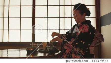 Tea, Japanese woman and traditional with a teapot, flavor and drinking ritual with herbal beverage and leaves. Asian person with culture and ceremony with Kimono, home and calming with wellness 111379454