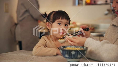 Family, japanese and woman feeding daughter in kitchen of home for growth, health or nutrition. Food, girl eating in Tokyo apartment with mother and grandparent for diet or child development Family, japanese and woman feeding daughter in kitchen of home for growth, health or nutrition. Food, girl eating in Tokyo apartment with mother and grandparent for diet or child development 111379474