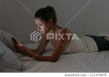 Girl chatting with her smartphone in bed at late night. Insomia and unhealthy sleep. Girl chatting with her smartphone in bed at late night. Insomia and unhealthy sleep. 111379676