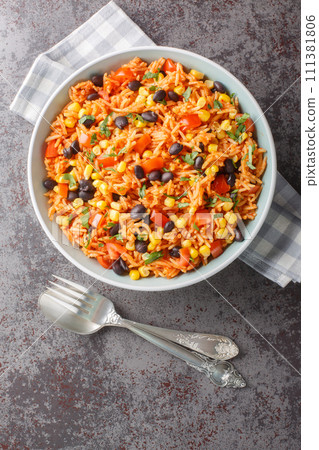 Delicious authentic Mexican tomato rice with black beans, onions and corn close-up in a bowl. Vertical top view 111381806