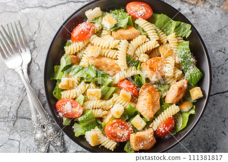 Chicken Caesar Salad with Pasta fusilli, romaine lettuce, parmesan, tomatoes and croutons close-up in a bowl. Horizontal top view Chicken Caesar Salad with Pasta fusilli, romaine lettuce, parmesan, tomatoes and croutons close-up in a bowl. Horizontal top view 111381817