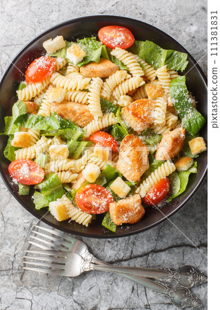 Caesar salad fusilli pasta with chicken, romaine lettuce, parmesan, tomatoes and croutons close-up in a bowl. Vertical top view Caesar salad fusilli pasta with chicken, romaine lettuce, parmesan, tomatoes and croutons close-up in a bowl. Vertical top view 111381831
