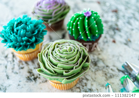 Using buttercream frosting, vanilla and chocolate cupcakes are intricately decorated to resemble various types of cactuses, creating a delightful and visually engaging dessert that showcases Using buttercream frosting, vanilla and chocolate cupcakes are intricately decorated to resemble various types of cactuses, creating a delightful and visually engaging dessert that showcases 111382147