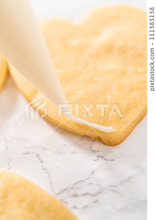 Decorating heart-shaped sugar cookies with pink and white royal icing for Valentine's Day. 111383138
