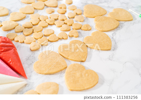Decorating heart-shaped sugar cookies with pink and white royal icing for Valentine's Day. Decorating heart-shaped sugar cookies with pink and white royal icing for Valentine's Day. 111383256