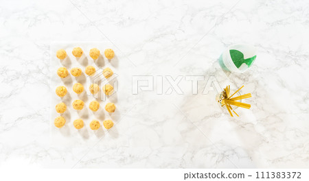 Flat lay. Dipping dough balls into green melted chocolate to make cactus cake pops for the Cinco de Mayo celebration. 111383372