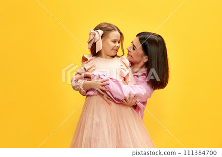 Happy, smiling, beautiful young woman hugging her adorable child, daughter against yellow studio background 111384700