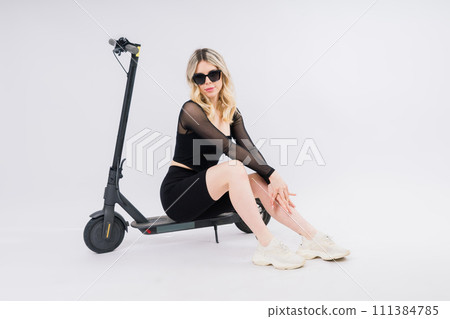 A blonde woman on red background sitting on electro scooter and resting, copy space 111384785