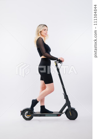 A blonde woman on red background sitting on electro scooter and resting, copy space 111384844