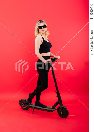 A blonde woman on red background sitting on electro scooter and resting, copy space A blonde woman on red background sitting on electro scooter and resting, copy space 111384848