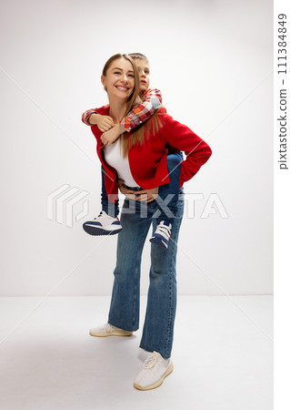 Happy, smiling young woman. mother playing with her little son, giving piggy back ride against white studio background. Casual style 111384849
