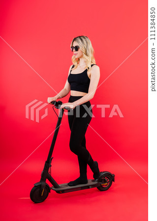 A blonde woman on red background sitting on electro scooter and resting, copy space 111384850
