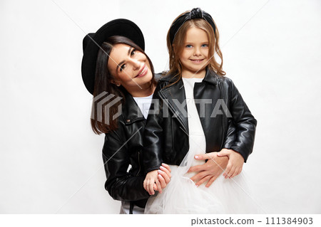 Beautiful young woman, mother posing with her little daughter on same style outfits against white studio background. Mother's day 111384903