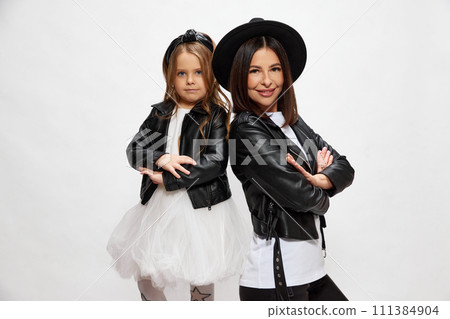 Beautiful young woman, mother posing with her little daughter on same style outfits against white studio background. Mother's day 111384904