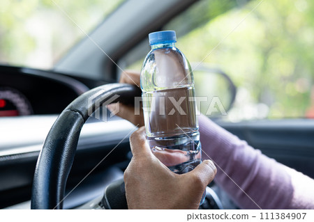 Asian woman driver holding bottle for drink water while driving a car. Plastic hot water bottle cause fire. 111384907
