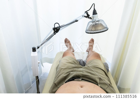 Patient receiving acupuncture treatment on legs and belly with infrared heater warming the treament area 111385516