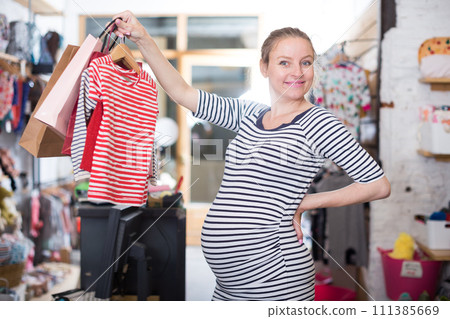 Pregnant woman in striped tunic chooses shirt in clothing shop 111385669