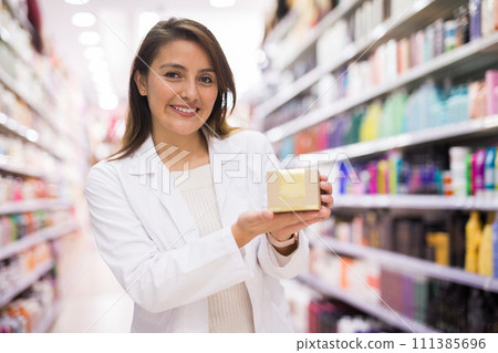 Smiling female seller demonstrating haircare cosmetics Smiling female seller demonstrating haircare cosmetics 111385696