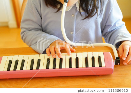 A 4th grade elementary school girl is playing a keyboard harmonica. 111386910