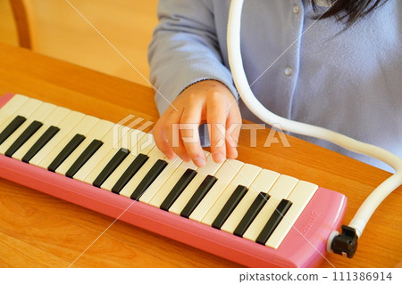 A 4th grade elementary school girl is playing a keyboard harmonica. 111386914