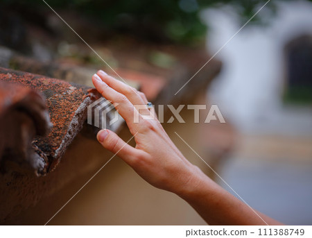 Female hand gently touches weathered tiles in old town of Kalechi, Antalya. tactile connection with ancient rooftops echoes rich history of surroundings Female hand gently touches weathered tiles in old town of Kalechi, Antalya. tactile connection with ancient rooftops echoes rich history of surroundings 111388749