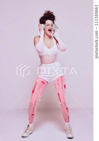 Stylish young woman listening to music in headphones and emotionally singing against pastel pink background. Online electronics store banner 111389661