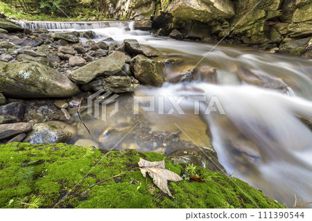 Fast flowing river stream with smooth silky water falling from big stones in beautiful waterfalls on bright sunny summer day. 111390544