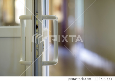 White plastic door detail with metal lock, handle and transparent glass on blurred interior background. Installation and design concept. 111390554