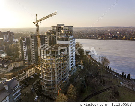 Apartment or office tall building under construction, top view. Tower crane and city landscape stretching to horizon. Drone aerial photography. Apartment or office tall building under construction, top view. Tower crane and city landscape stretching to horizon. Drone aerial photography. 111390598
