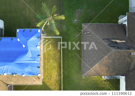 Top view of leaking house roof covered with protective tarp sheets against rain water leaks until replacement of asphalt shingles. Damage of building rooftop as aftermath of hurricane Ian in Florida 111390612